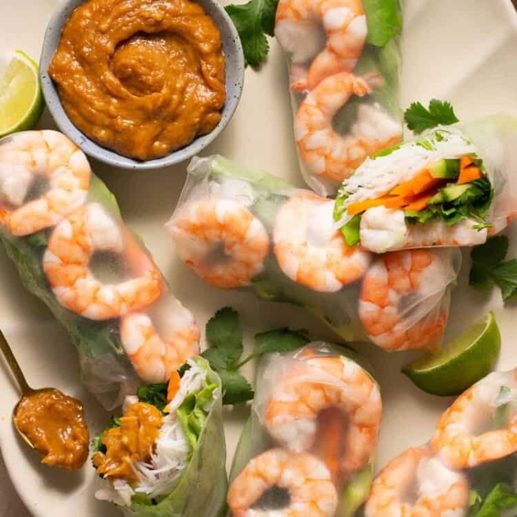 Several rice paper rolls on a platter with peanut sauce.