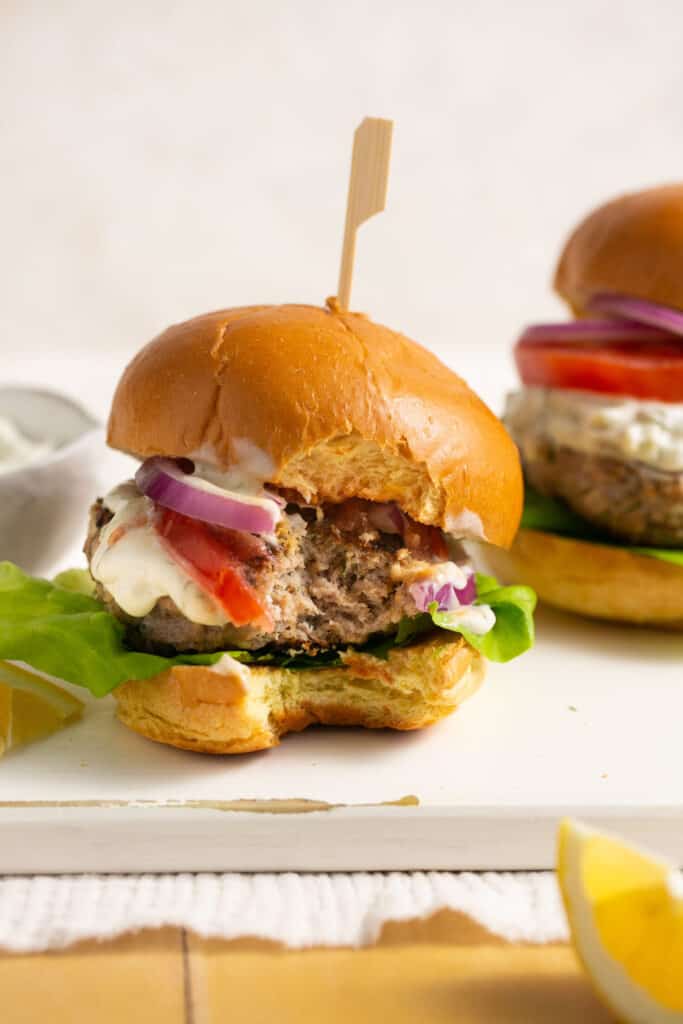 Greek style air fryer turkey burgers on buns with tomato, red onion, lettuce,  and tzatziki.