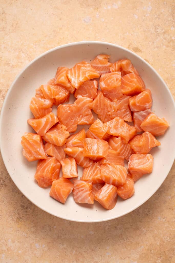 Raw salmon cut into small pieces on a plate.