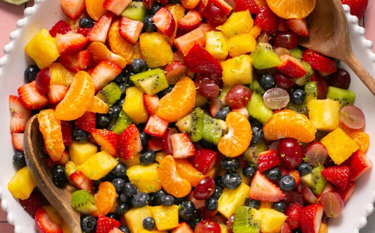 Rainbow fruit salad with honey lime dressing in a serving bowl with a spoon.