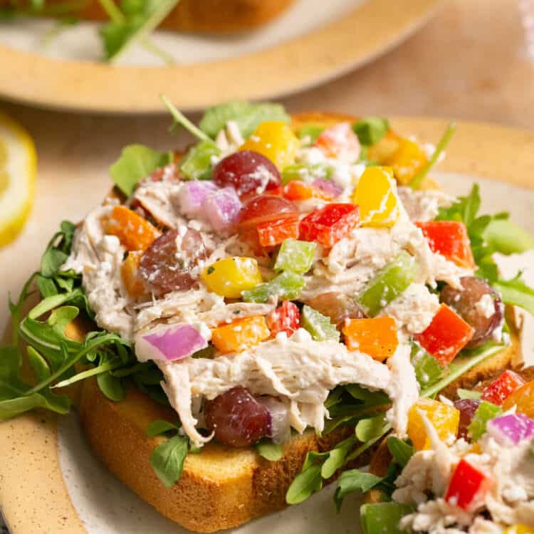 Rainbow chicken salad on two pieces of toast and greens in a plate.
