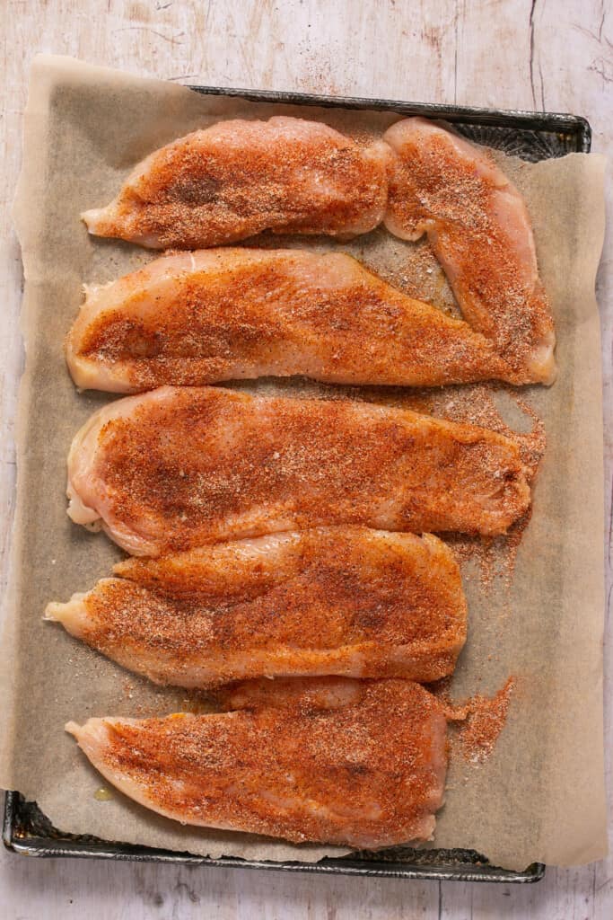 Raw chicken tenderloins spinkled with seasoning.