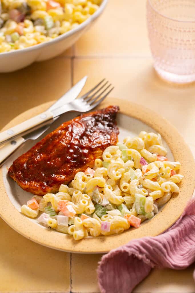 Healthy macaroni salad (deli style) in on a plate with piece of cooked chicken.