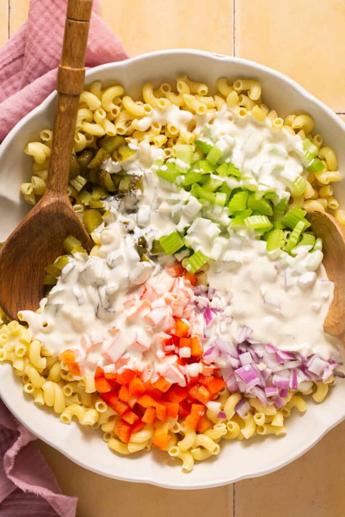 Macaroni, veggies, and dressing in a large bowl before being mixed together.