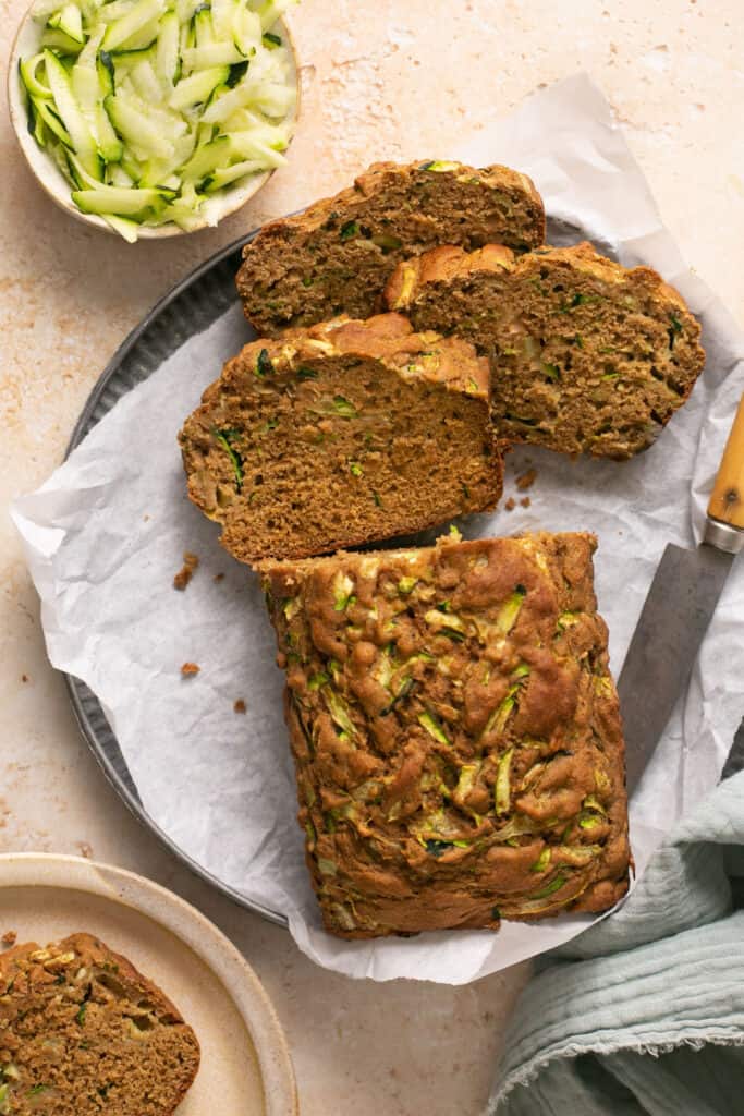 Healthy zucchini bread, half of it cut into slices, on a plate with parchment paper and a knife.