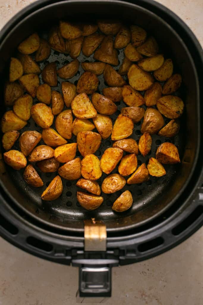 Yukon poatoes cut into quarters in an air fryer after being cooked.