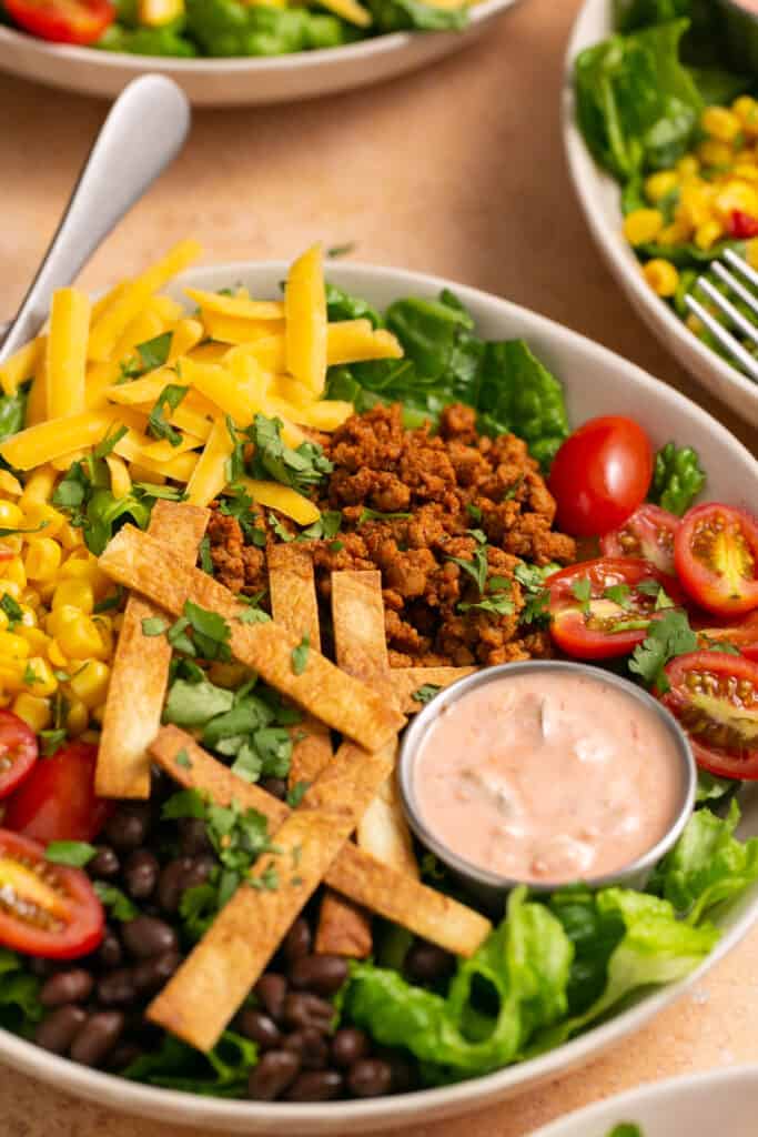 Zoomed in view of healthy taco salad with ground turkey in bowl with a fork with salsa yogurt dressing on the side.