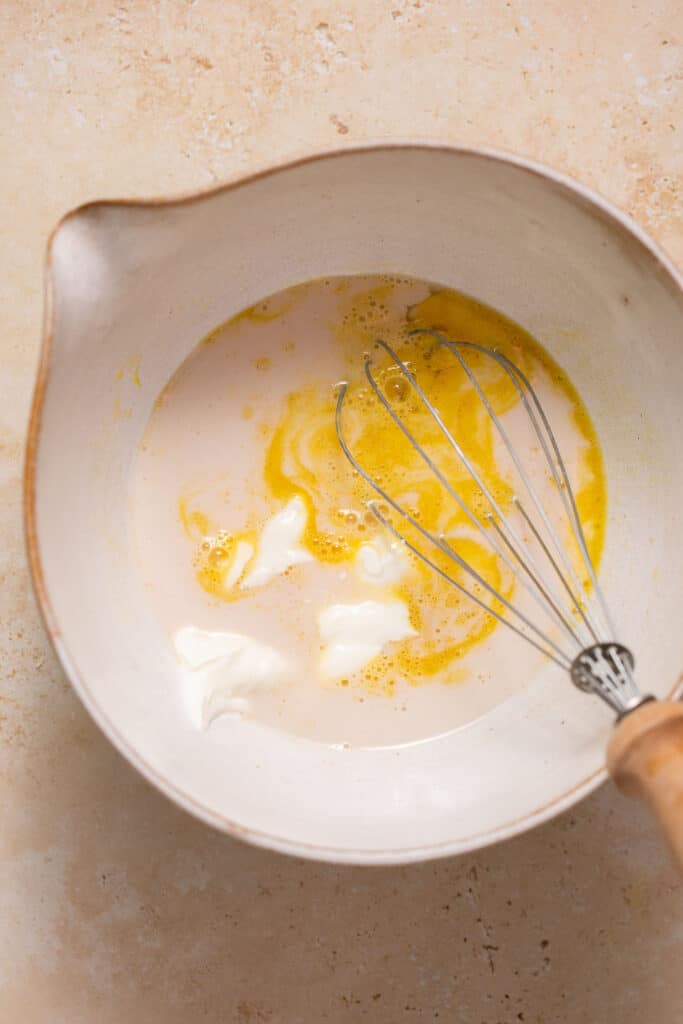 Wet ingredients for low carb lemon poppy seed muffins in a mixing bowl with a whisk.
