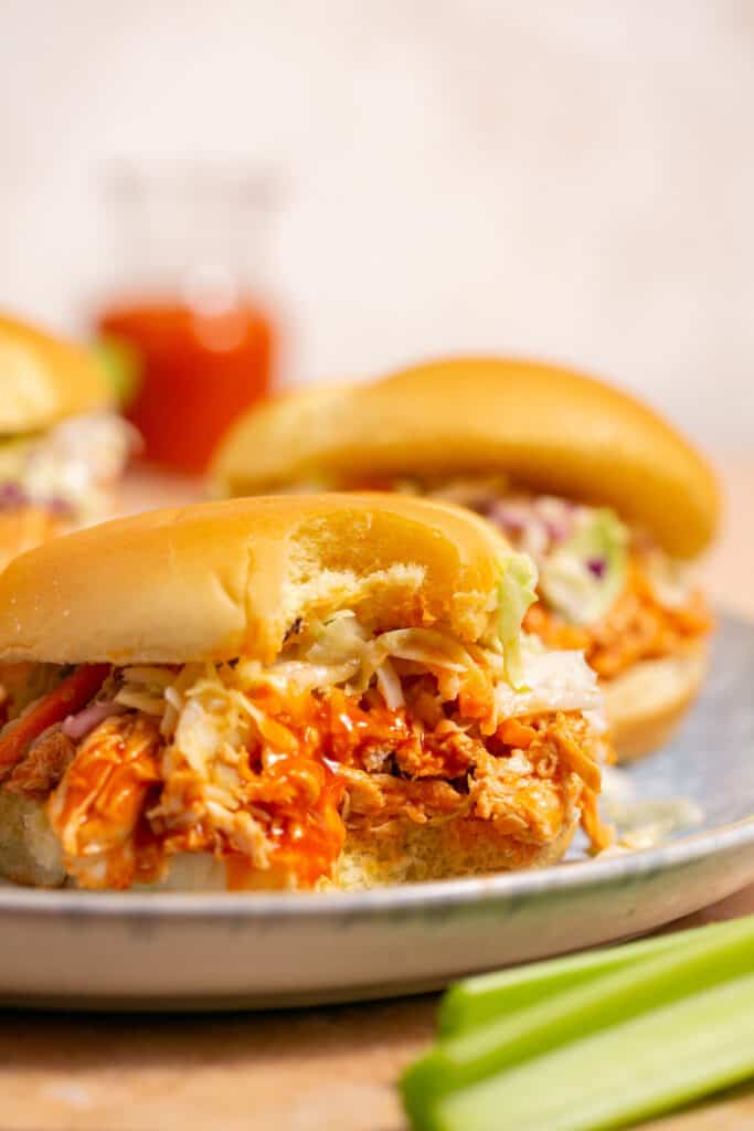 Zoomed in view of pulled buffalo chicken topped with coleslaw on a bun on plate. 