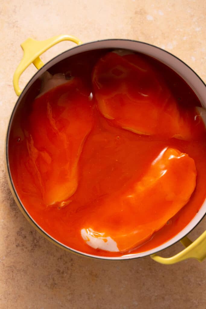 Raw chicken breasts covered with buffalo sauce in a pot.