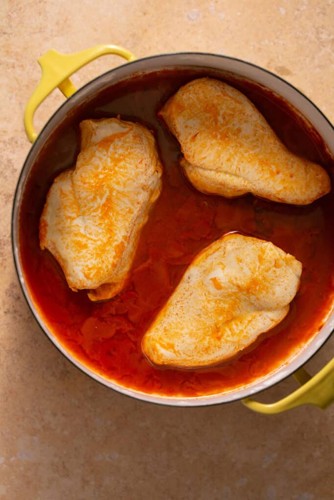 Cooked chicken breasts in a pot with buffalo sauce.