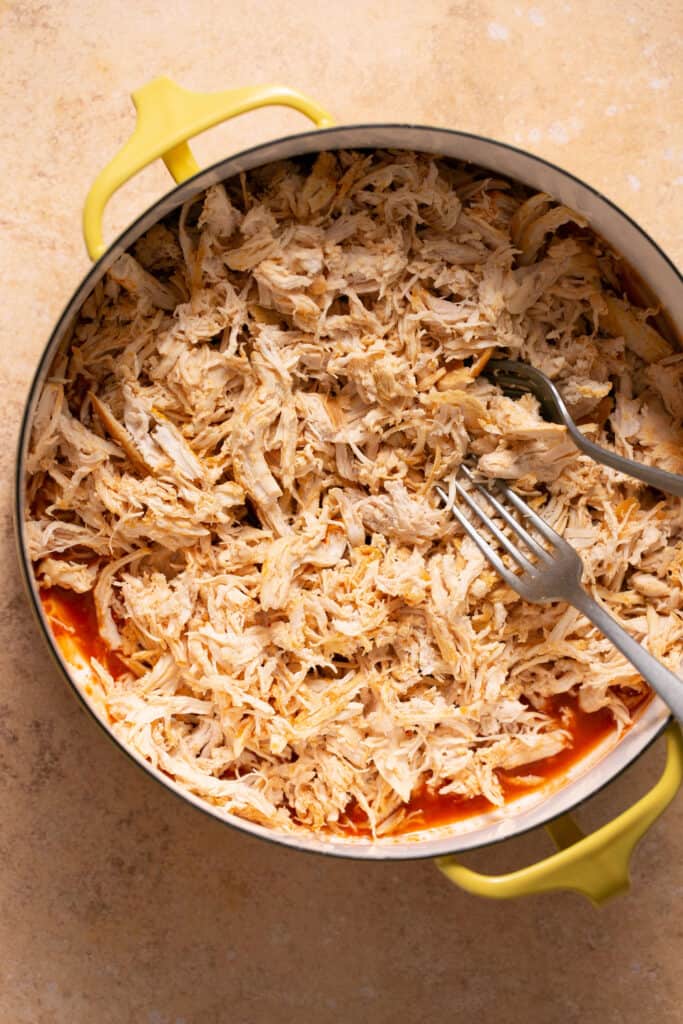 Cooked shredded chicken on top of buffalo sauce in a pot.