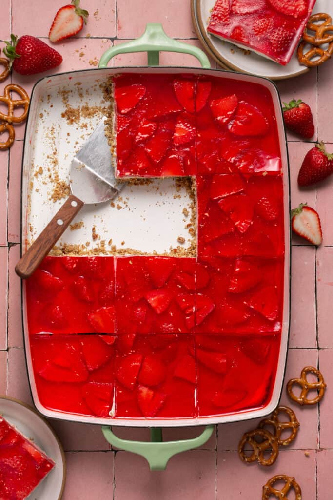 Pan of Low Sugar Strawberry Pretzel Jello Salad dessert in 9x13 pan with 3 pieces missing and pie cutter.