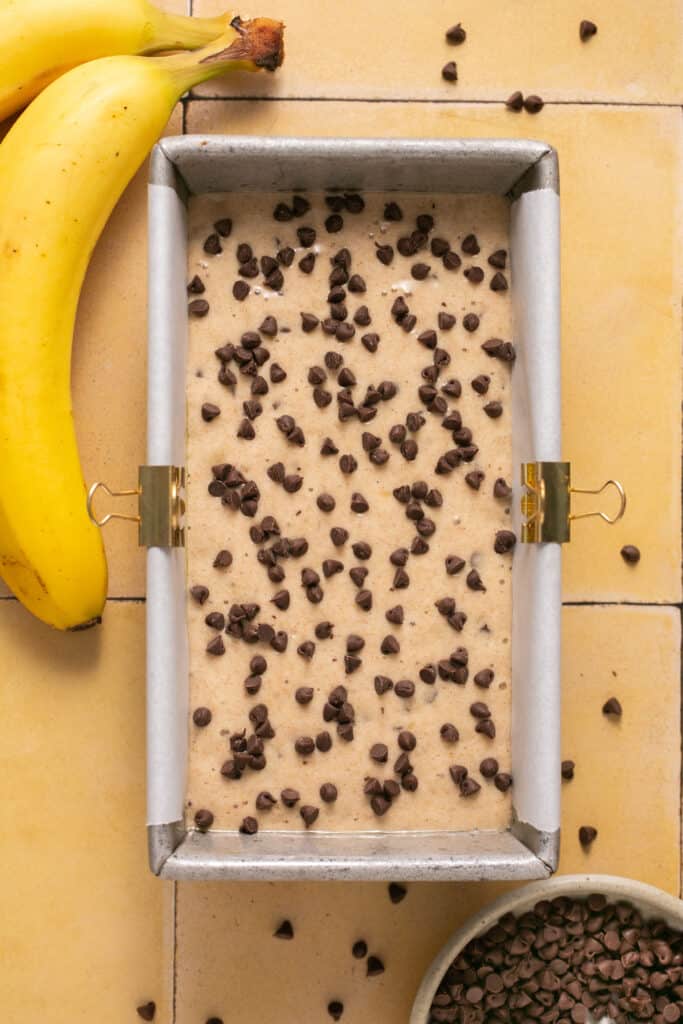 Skinny chocolate chip banana bread batter topped with chocolate chips in a loaf pan.