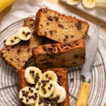 Slices of skinny chocolate chip banana bread on a plate with banana slices and chocolate chips.