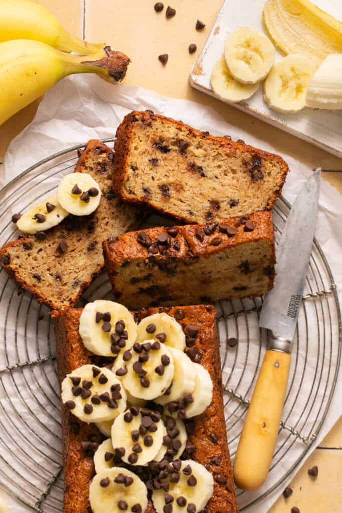 Sliced skinny banana bread with chocolate chips on a plate with banana slices and more chocolate chips.