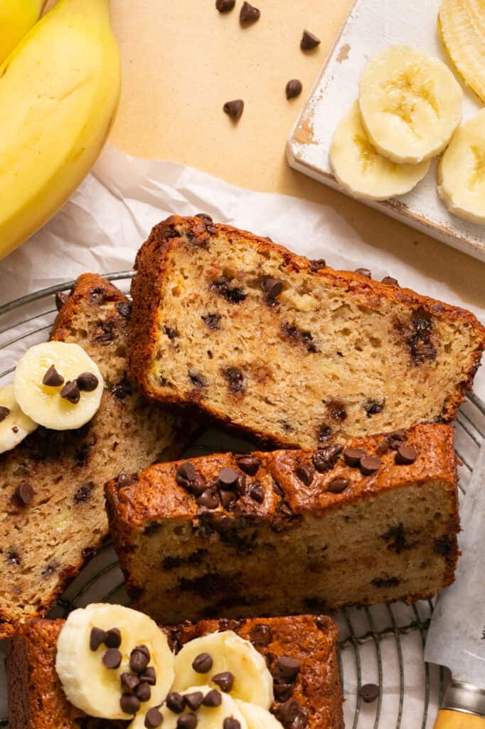 Sliced skinny banana bread with chocolate chips on a plate with banana slices and more chocolate chips.