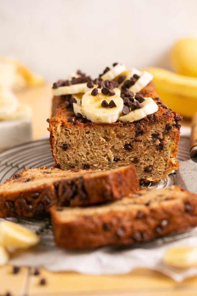 Sliced skinny banana bread with chocolate chips on a plate topped with banana slices and more chocolate chips.