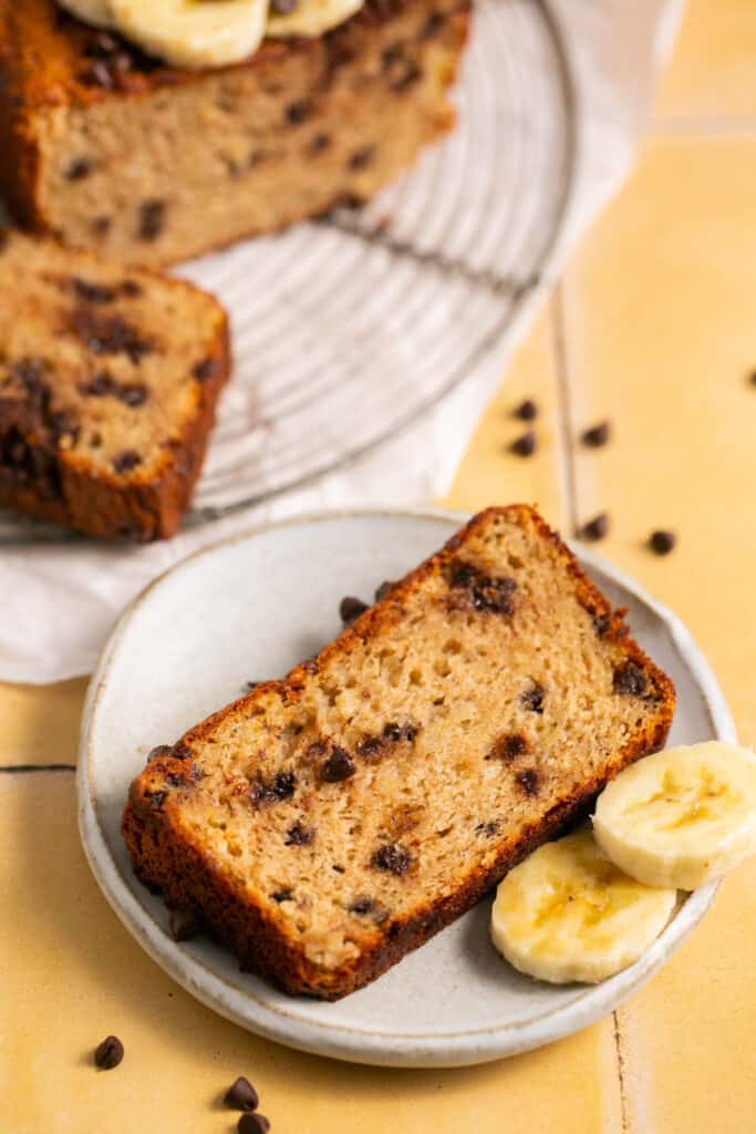 Skinny banana bread with chocolate chips on a plate with sliced bananas.