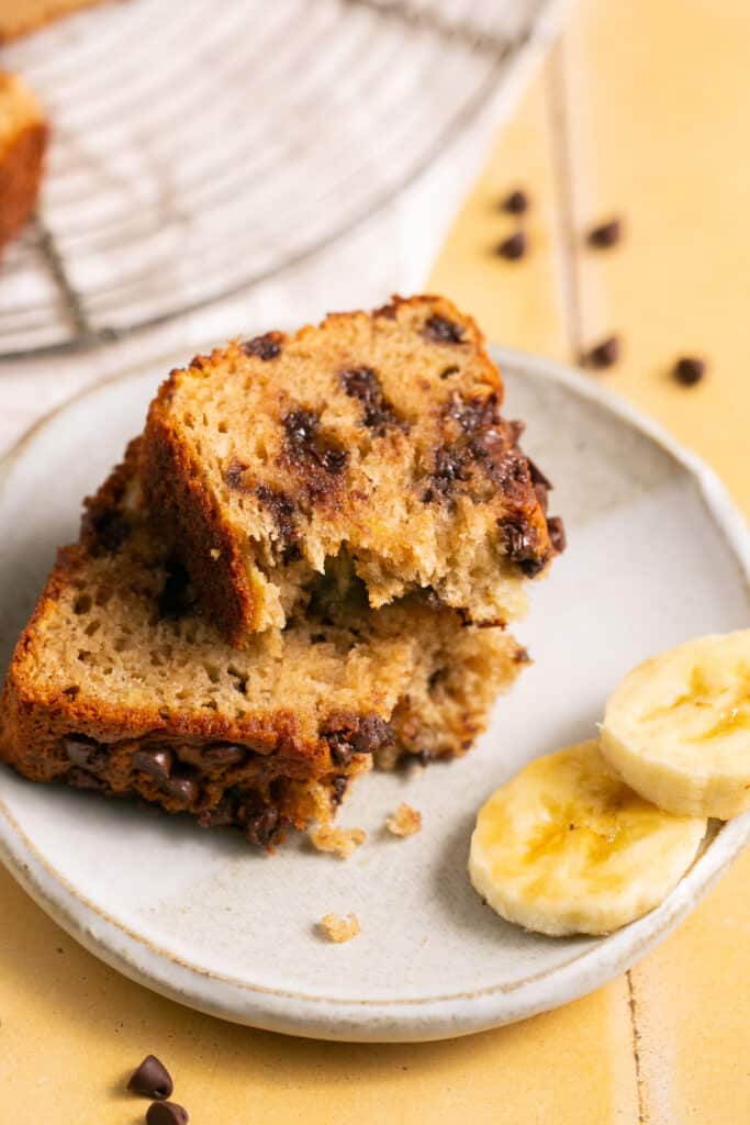Skinny chocolate chip banana bread cut in half on a small plate garnished with banana slices.