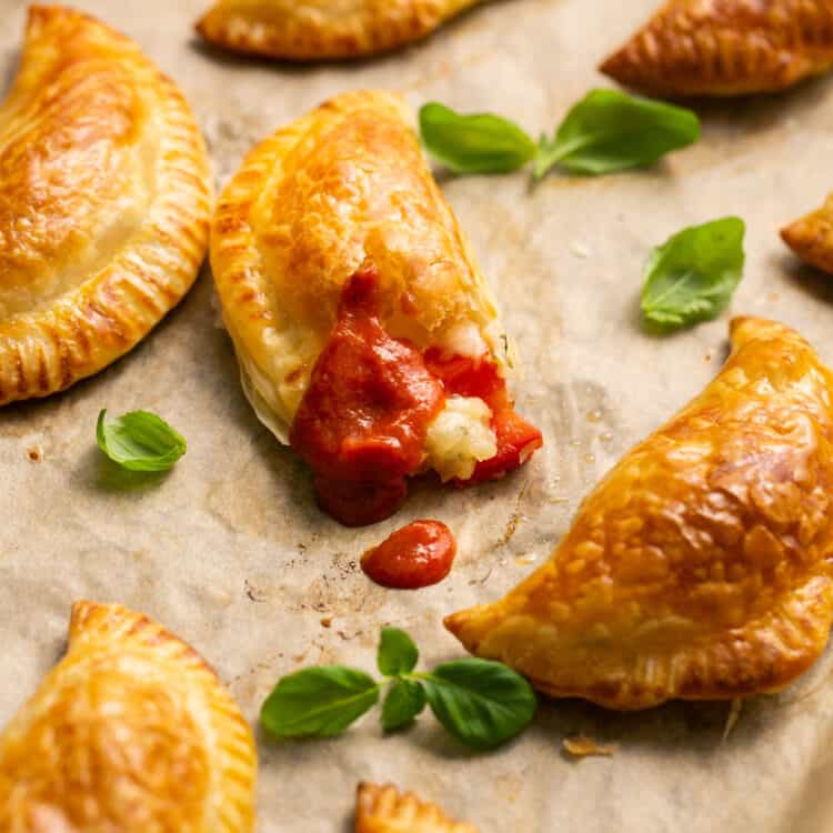 Caprese empanadas on parchment paper dipped in marinara sauce.