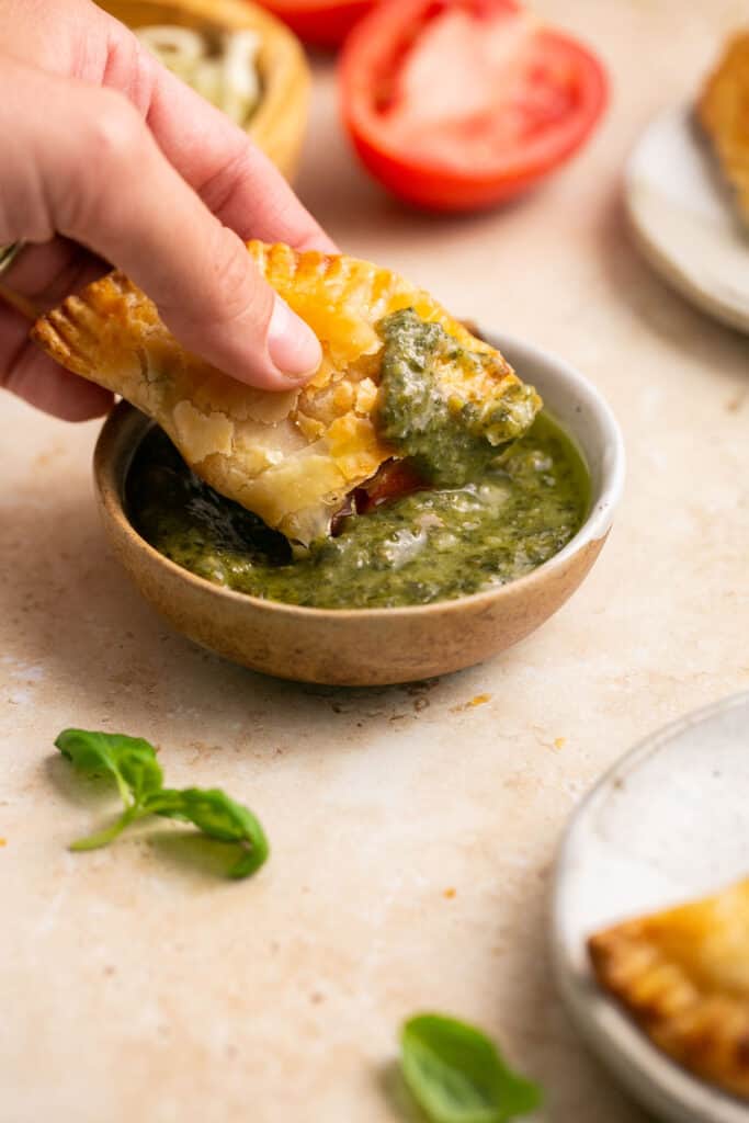 Caprese empanada being dipped into a small bowl of pesto.