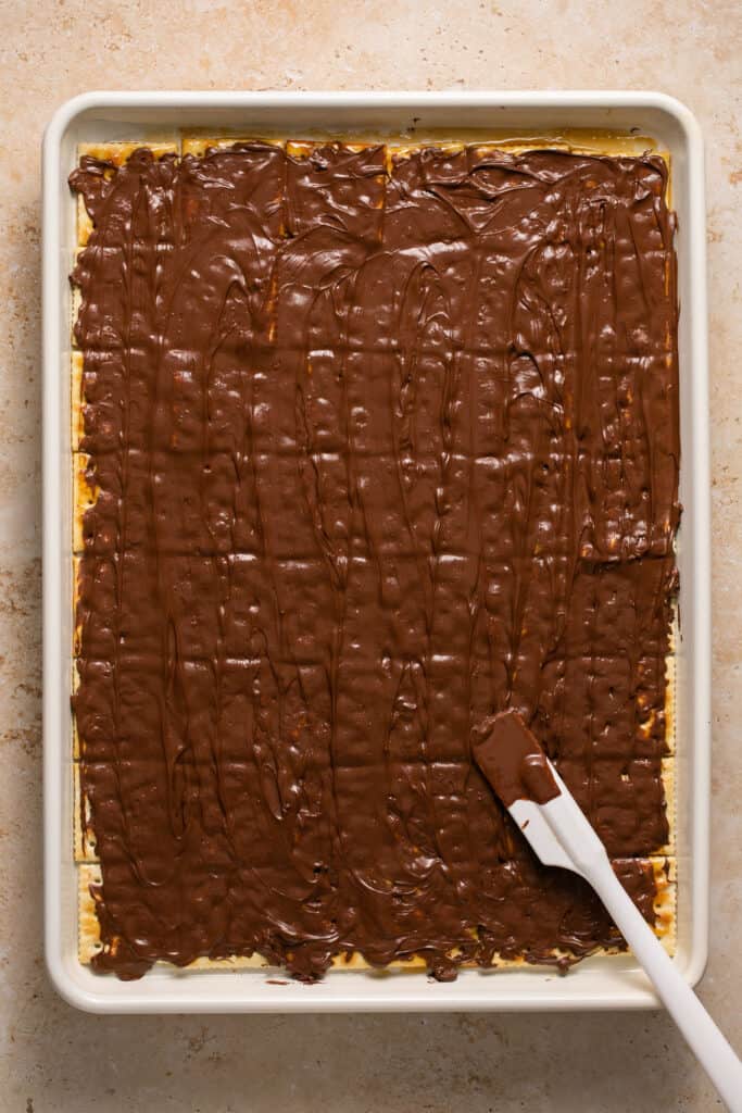 Melted chocolate chips being spread on top of the layer of crackers.