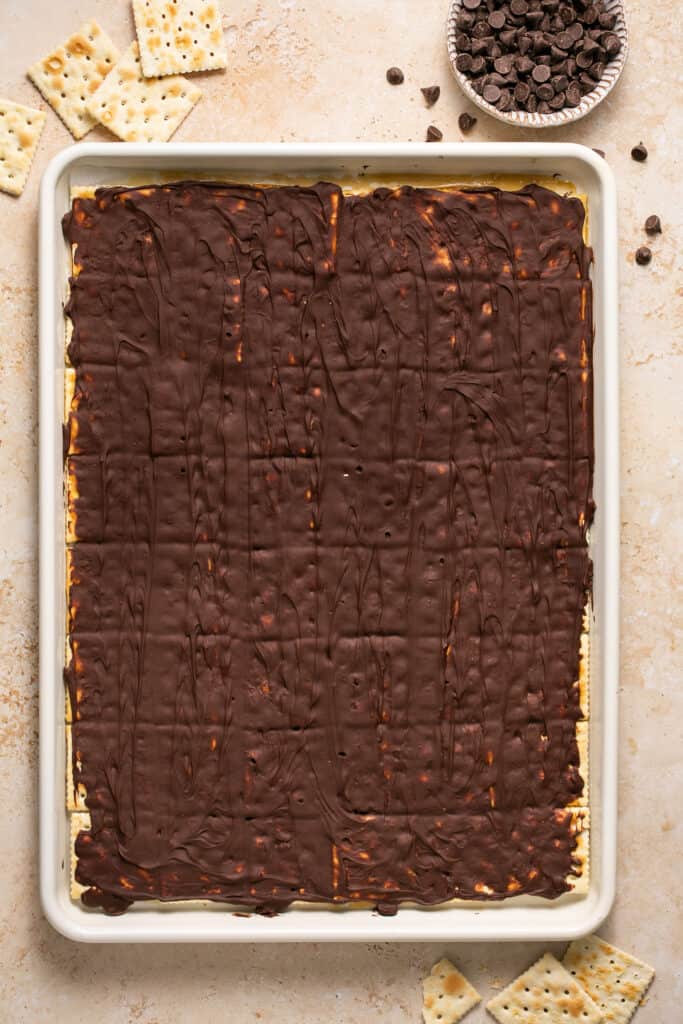 Melted chocolate on top of the later of crackers on a baking sheet.