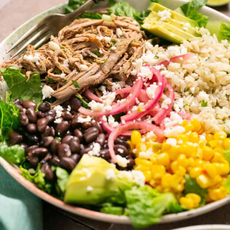 Zoomed in view of carnitas burrito bowls in bowls with forks.