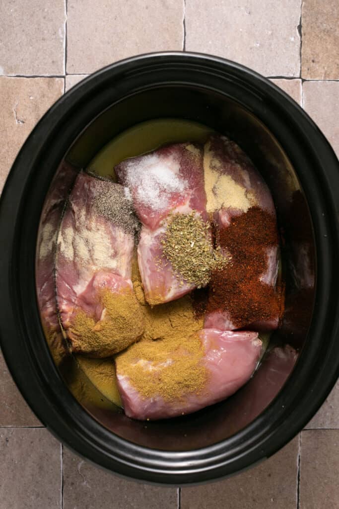 Raw pork topped with spices in a slow cooker.