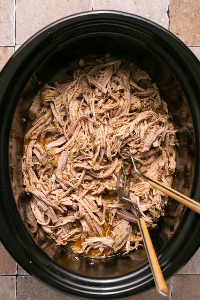 Shredded pork with two forks in a slow cooker.