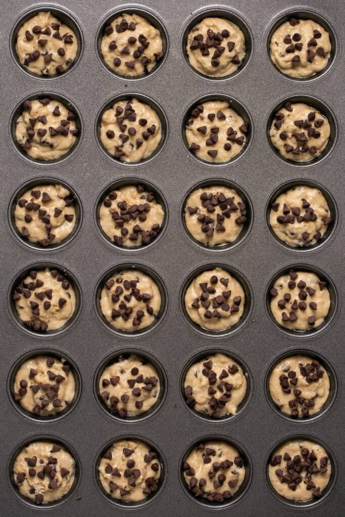 Mini chocolate chip pancake bites in a mini muffin tin before being baked with additional chocoalte chips sprinkled on top.