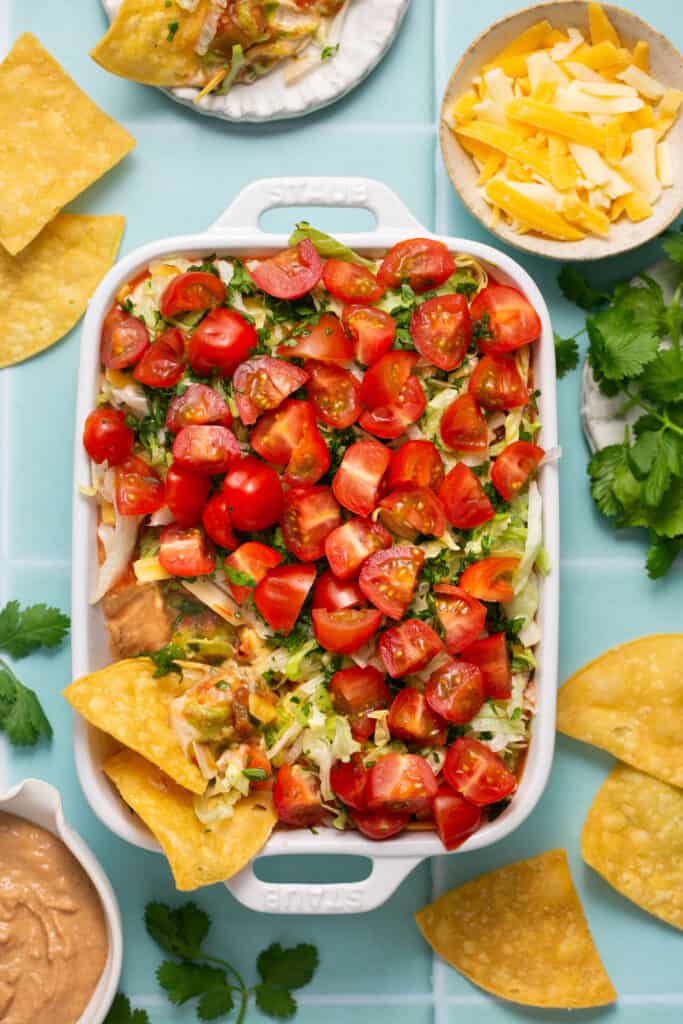 Healthy 7 layer dip in baking dish with a few tortilla chips dipped in it. 