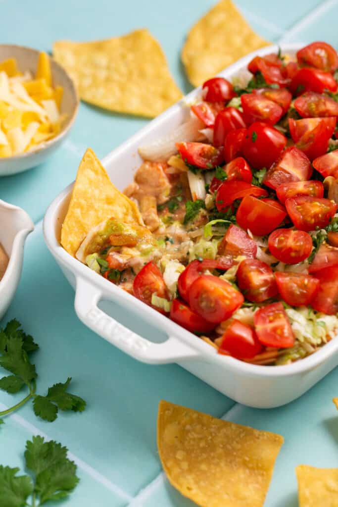 Zoomed in view of healthy 7 layer dip in baking dish with a few tortilla chips dipped in it. 