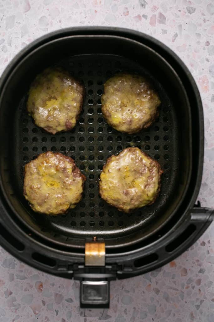 Air fryer burgers topped with the butter mixture in an air fryer basket.