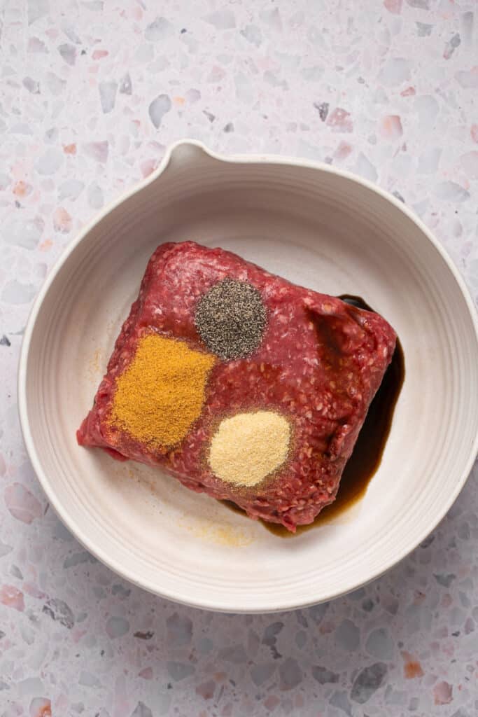 Raw groun beef with seasonings in a bowl.