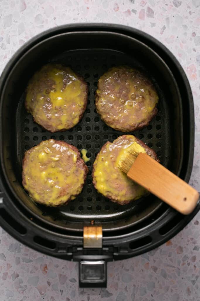 Butter mixture being put on top of the burger patties in the air fryer basket.