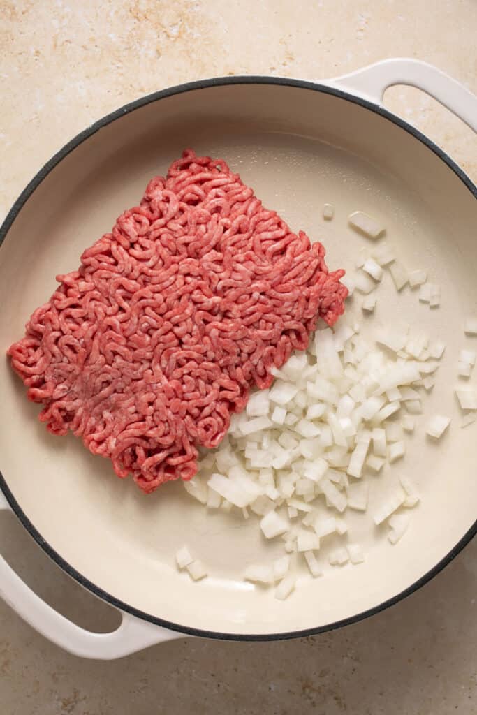 Raw ground beef and chopped onion in a skillet.