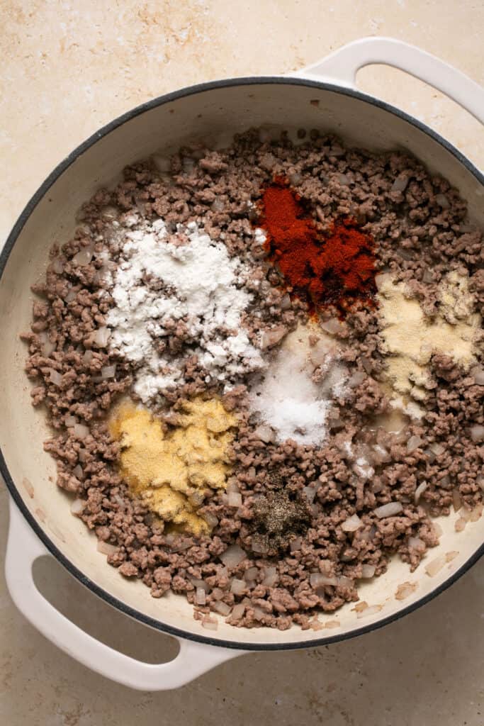 Spices sprinkled over cooked ground beef in a skillet.