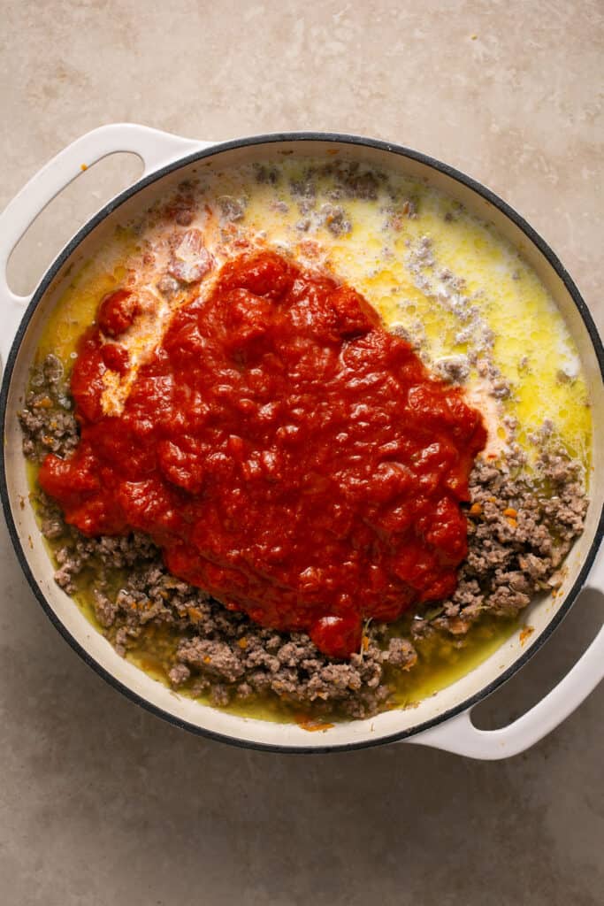 Pasta sauce added to the cooked ground beef mixture in a skillet.