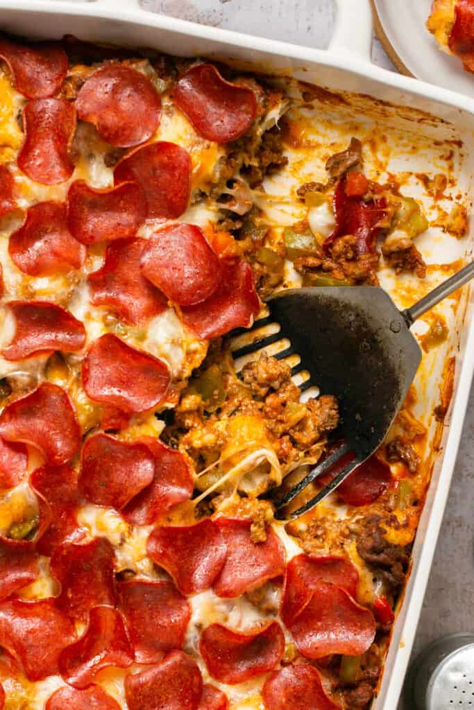 Pizza casserole with biscuits being served out of a baking dish.