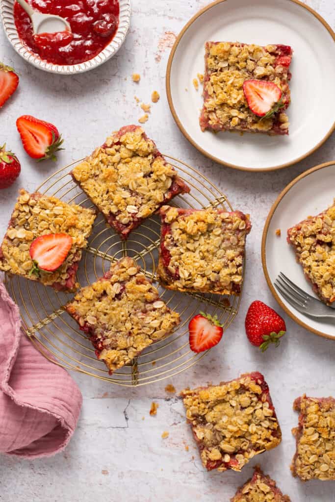 Healthy strawberry crumble bars, some on a cooling rack, some on small plates with forks.