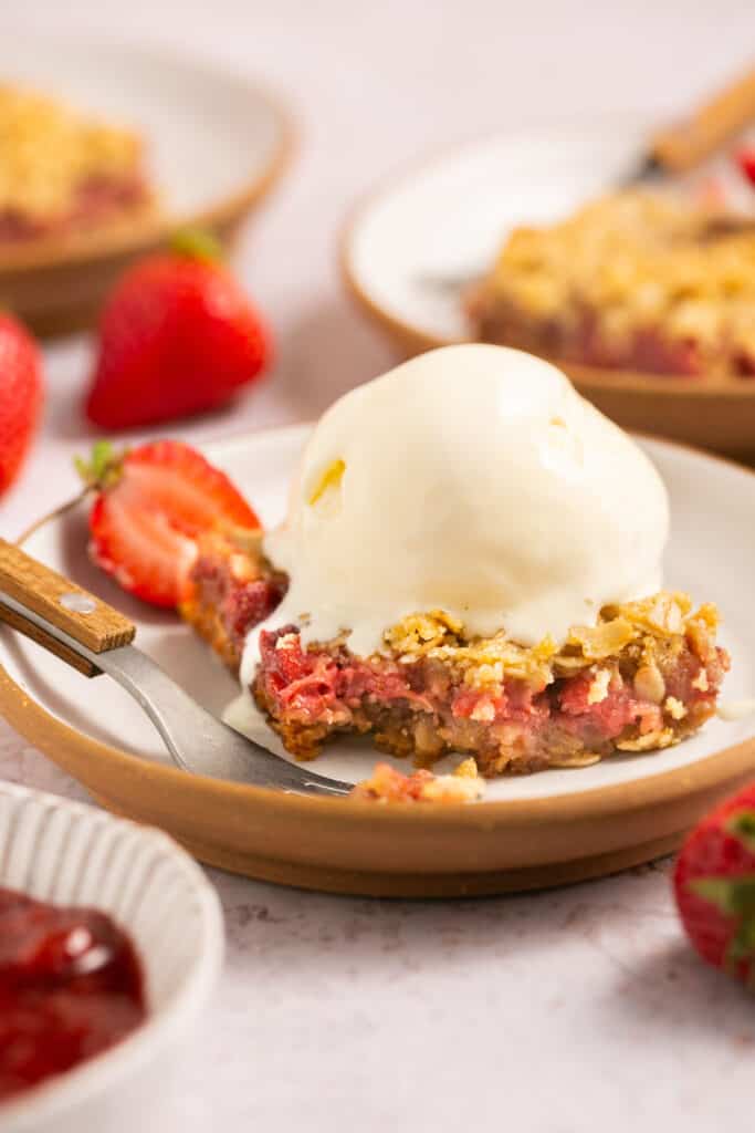 Healthy strawberry crumble bar topped with vanilla ince cream on a plate with a fork.