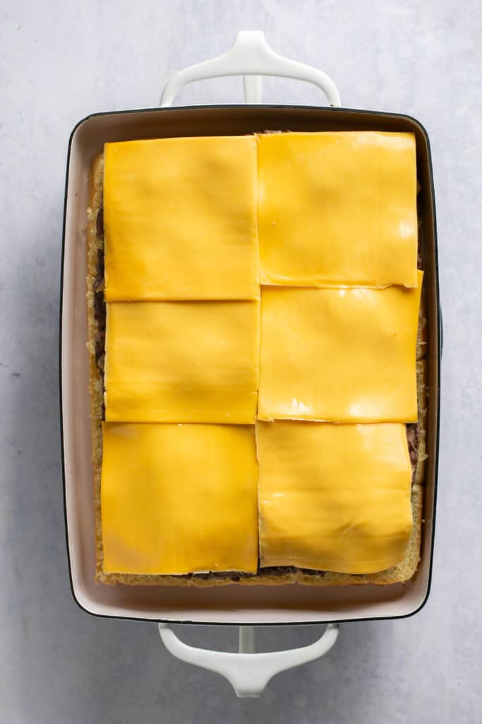 Ground beef topped with slices of cheese in a rectangle baking dish.