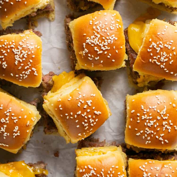 Overhead view of cheeseburger sliders with hawaiian rolls on parchment paper.