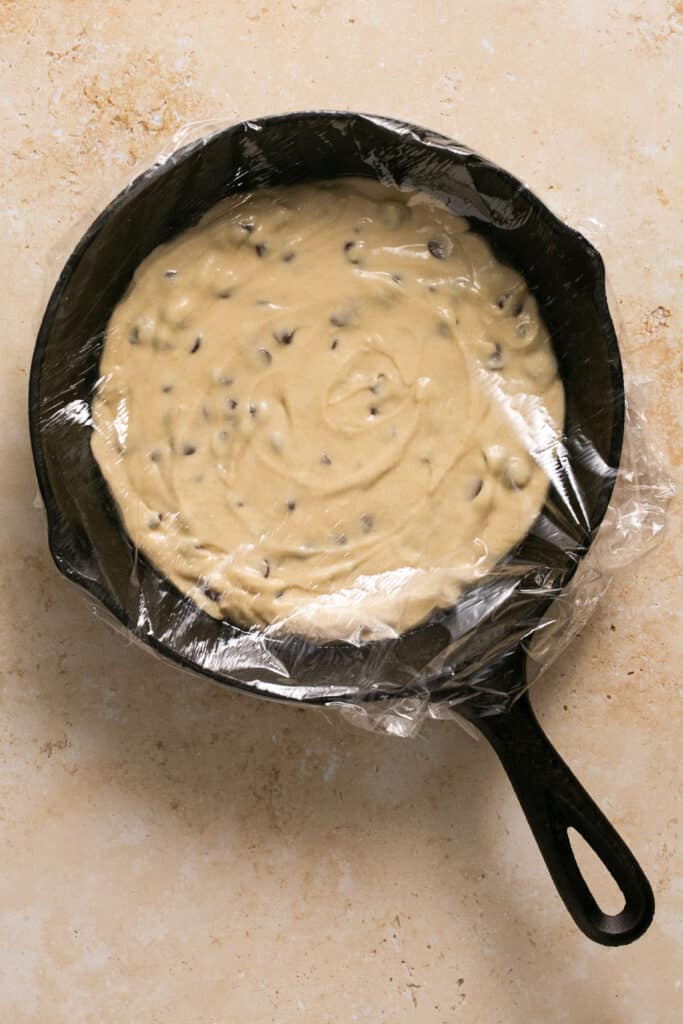 Batter for protein skillet cookie in a skillet covered with plastic wrap.