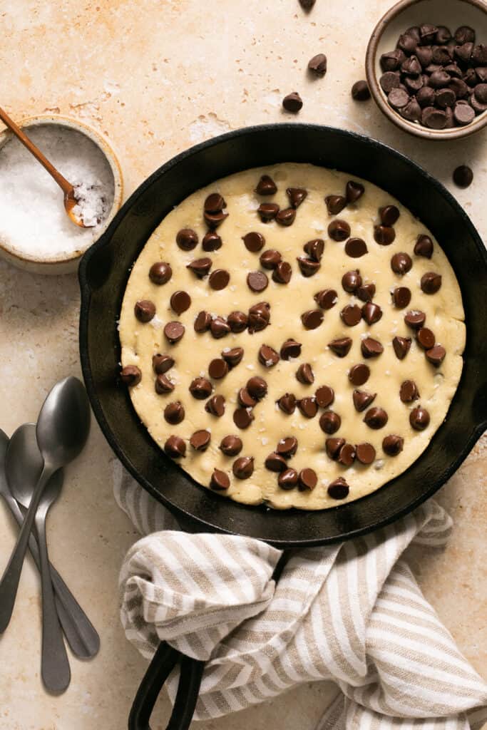 Protein skillet cookie with melty chocoalte chips in a skillet with spoons on the side.