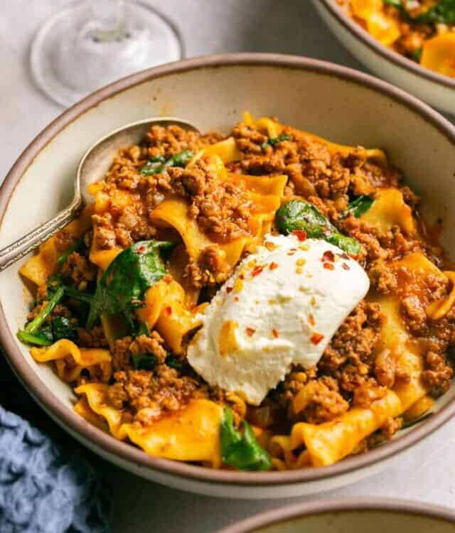 Crock pot lasagna coup in a bowl with a spoon topped with a dollop of a creamy cheese blend.