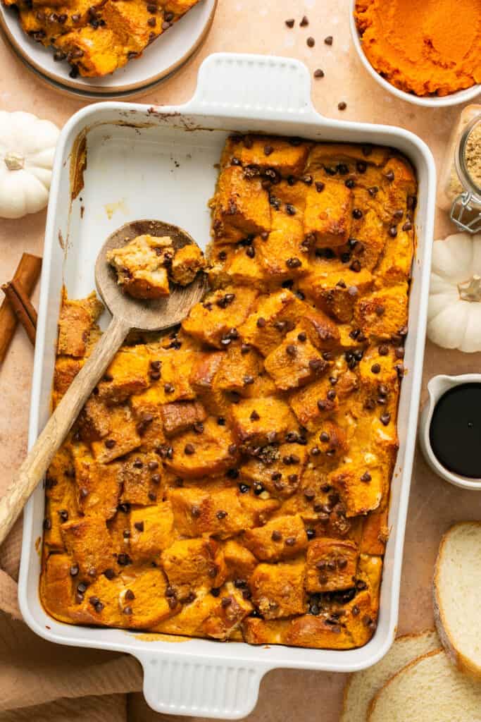Pumpkin chocolate chip protein french toast bake in a baking dish being served with a wooden spoon.