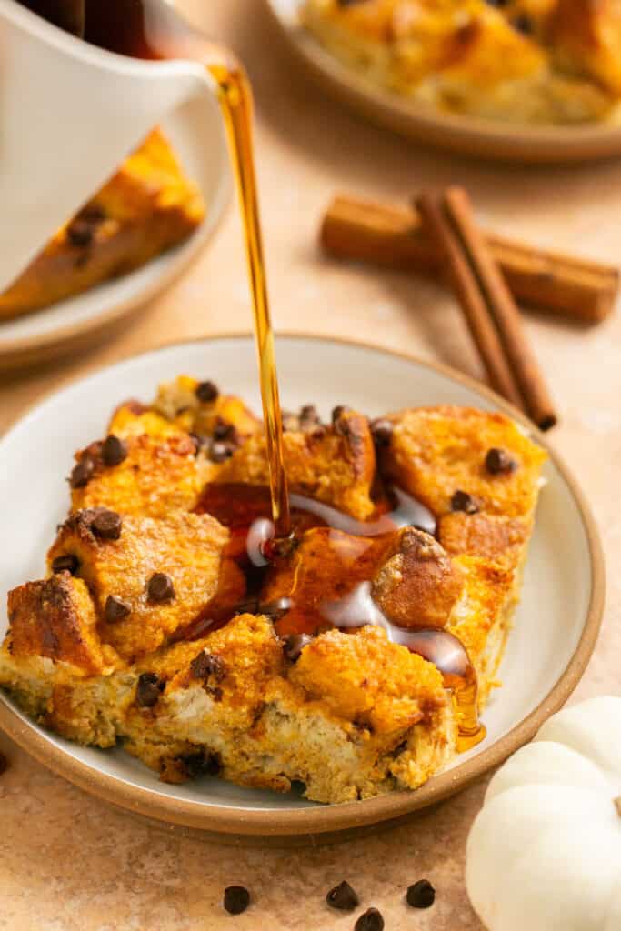 Pumpkin chocolate chip protein french toast bake on a small plate being drizzled with maple syrup.